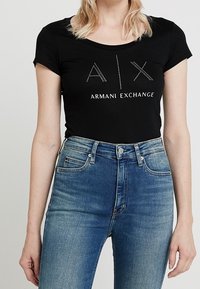 Černé bavlněné tričko s krátkými rukávy a kulatým výstřihem, zdobené kamínkovým logem "A|X ARMANI EXCHANGE". Slučuje se s modrými skinny džíny.