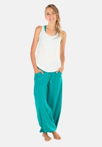 Top blanco de tirantes con un ligero arco en el dobladillo, combinado con pantalones sueltos color turquesa que tienen cordón elástico y bolsillos laterales.