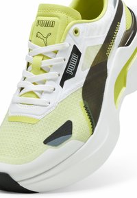 Sneaker Puma in rete gialla e bianca con accenti neri, suola arrotondata e sistema di allacciatura prominente. Caratteristiche includono sovrapposizioni testurizzate e logo.