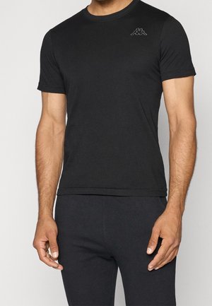 Mann trägt ein einfaches schwarzes Kurzarm-T-Shirt mit kleinem Logo auf der linken Brust und dazu passende schwarze Hose.