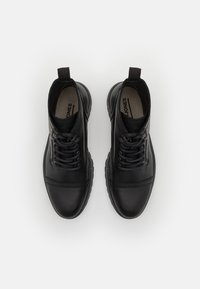 Botas de tobillo de cuero negro con puntera redonda, cordones en la parte delantera y lengüetas de tiro. Presentan acentos cosidos y una suela de goma para mayor tracción.
