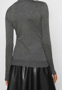 Maglione grigio scuro con maniche lunghe e orlo a coste, realizzato in morbido materiale a maglia, indossato sopra una gonna di pelle nera.