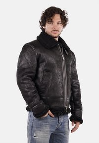 Bomber jacket in shearling nera con colletto in morbido pelo, due tasche frontali e chiusura con zip, caratterizzato da una finitura in pelle opaca e testurizzata.