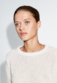 Sweter dziany w miękkim kremowym kolorze, z okrągłym dekoltem i lekką, przewiewną fakturą z delikatnymi otworami w materiale.