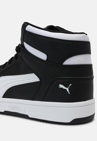 Baskets montantes Puma noir et blanc avec semelle blanche, logo Puma au talon et sur le côté, coutures visibles et col de cheville rembourré.
