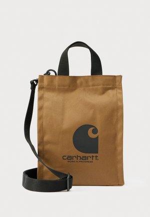 Καφέ ορθογώνια τσάντα tote Carhartt με μαύρο λογότυπο, κοντές λαβές και αποσπώμενο ρυθμιζόμενο μαύρο ιμάντα ώμου σε λευκό φόντο.