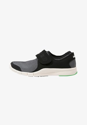 Baskets slip-on grises et noires avec bride velcro réglable, semelle blanche et accent vert au talon, conçues pour le confort et un usage décontracté.