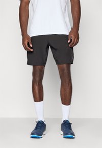 Sorte træningsshorts med elastisk talje, parret med hvide sokker og marineblå sportssko. Glat tekstur, ingen synlige mønstre.
