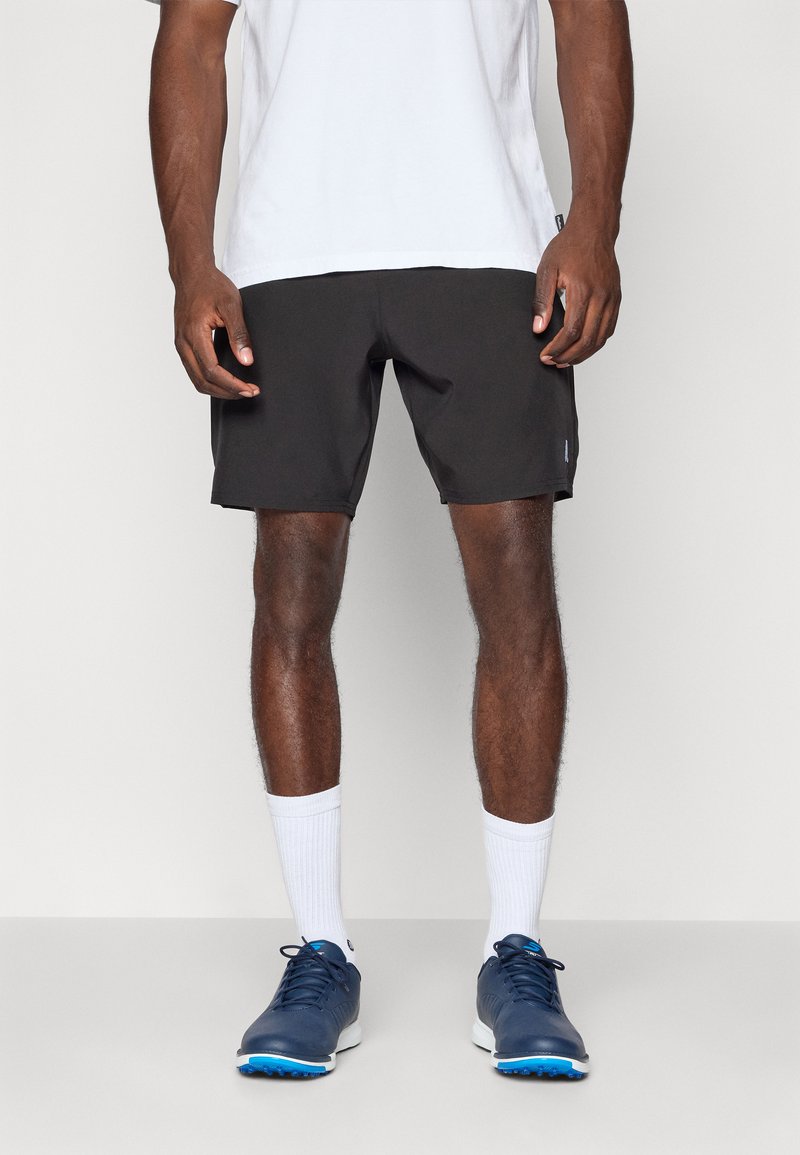 Sorte træningsshorts med elastisk talje, parret med hvide sokker og marineblå sportssko. Glat tekstur, ingen synlige mønstre.