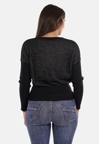 Maglione nero con un retro testurizzato dall'aspetto luccicante, polsini e orlo a costine, abbinato a jeans blu con tasche posteriori.