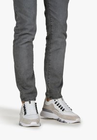 Białe i szare sneakersy z mieszanym materiałowym wzornictwem, z teksturowaną cholewką, wzmocnionymi oczkami i masywną gumową podeszwą.
