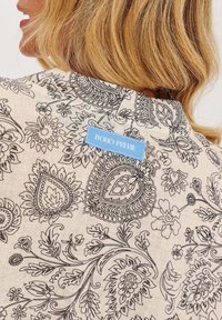 Boho prérie top v béžovej látke s čiernymi paisley a kvetinovými vzormi. Štítok viditeľný na zadnej strane s názvom značky v modrej.