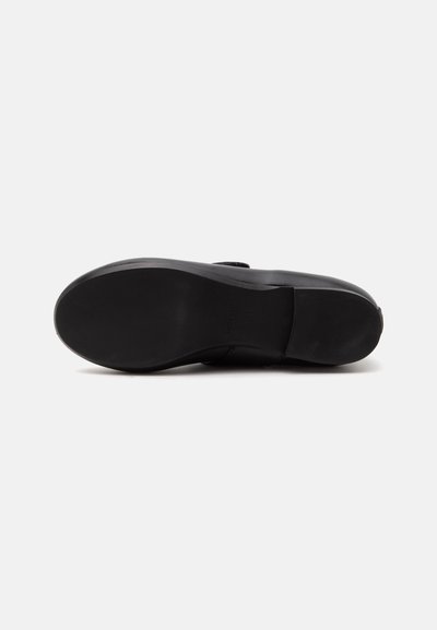 Semelle d'une chaussure habillée en cuir noir vue de dessous, avec une surface lisse, solide et un petit talon sur un fond uni.