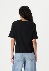Svart kortermet topp med avslappet passform og rund hals, brukt sammen med lyseblå høyhalkede jeans, som viser et enkelt design.