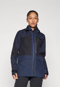 Marineblaue wasserdichte Jacke mit Kapuze, die kontrastierende strukturierte Einsätze, Reißverschlusstaschen und verstellbare Bündchen für einen sicheren Sitz bietet.