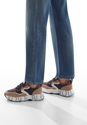 Sneaker sportive caratterizzati da un mix di materiali neri, marroni e bordeaux, con accenti testurizzati e una suola bianca con scritte audaci stampate.