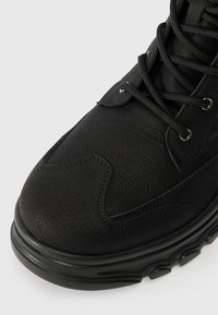 Melni potīšu zābaki ar teksturētu ādas virsu, apaļu purngalu, mīkstu apkakli un izturīgām melnām șņorēm ar metāla acīm. Sānu dūriena detaļa.