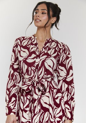 Abito con motivo floreale in bordeaux e avorio, dotato di colletto, chiusura a bottoni e vita sagomata. Maniche lunghe con polsini aderenti.