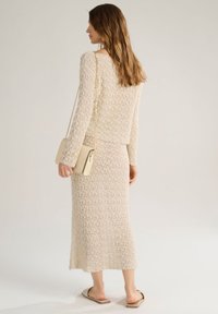 Set di due pezzi beige in maglia caratterizzato da un design a trama aperta e testurizzata, con una maglia a maniche lunghe e una gonna aderente. Borsa beige minimalista e sandali.