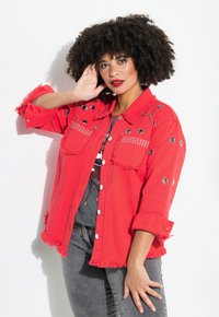 Chaqueta de mezclilla roja con bordes deshilachados, ojales plateados y acentos de strass, que cuenta con un cierre frontal de botones y bolsillos en el pecho.