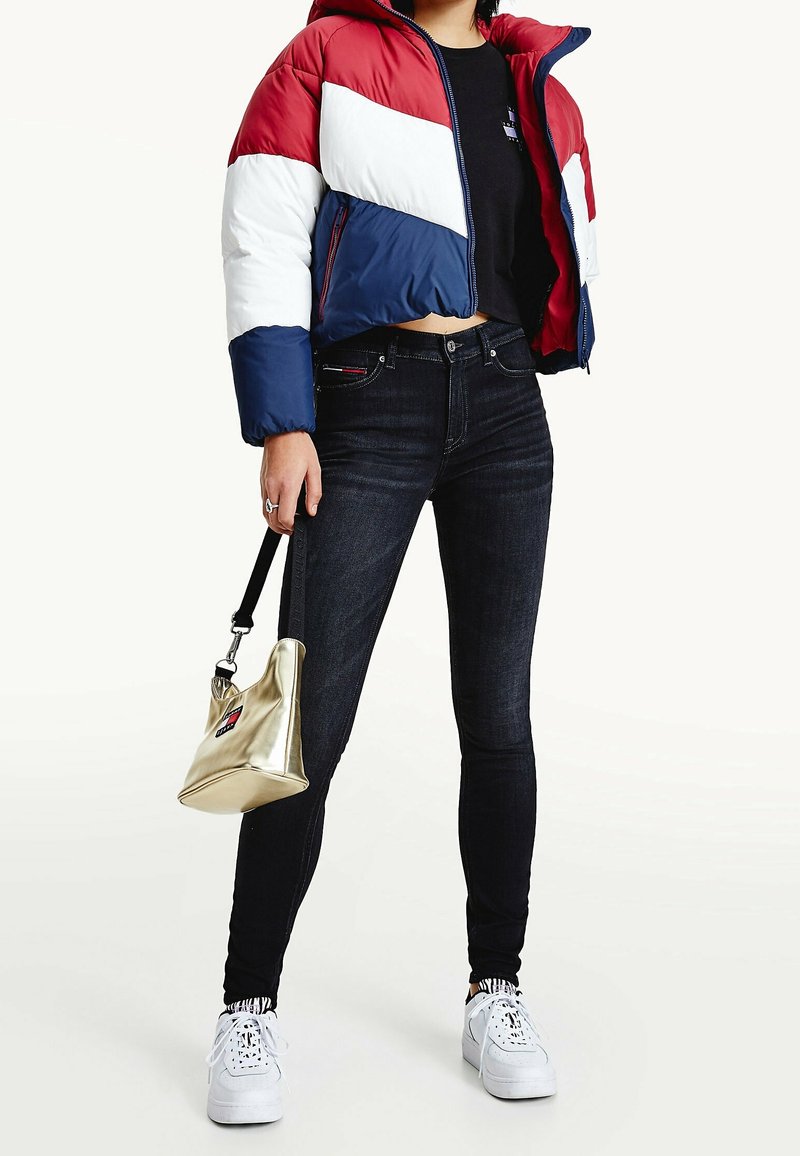 Röd, vit och blå puffjacka, svarta tajta jeans, vita sneakers och en metallisk guldhandväska med axelrem. Informella kläddetaljer synliga.