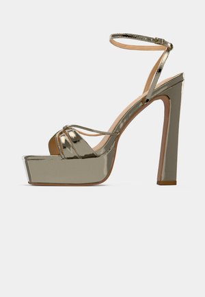 Metalen gouden platform sandaal met een blokhak, open teen en enkelband. Kenmerkt zich door crisscross-details aan de voorkant en een gladde afwerking.