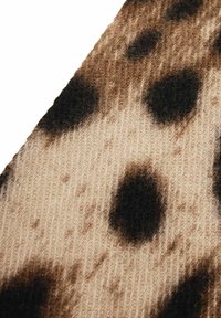 Strickstoff mit beigem Hintergrund und großen, dunkelbraunen Flecken. Die Textur wirkt weich mit einem leichten Glanz und zeigt ein lässiges Muster.