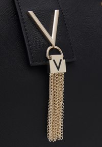 Svart handväska med texturerad yta, guldmaterial med en "V"-logotyp som accent och en dekorativ kedjeöron.