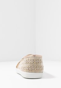 Chaussures slip-on en textile avec un motif tissé beige et or, des accents rose doré doux, et une semelle en caoutchouc blanche. Vue arrière mettant en valeur la texture et la forme.
