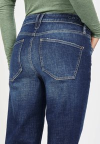 Dark blue denim jeans with a high waist, two back pockets, and subtle fading details. The material has a smooth texture.