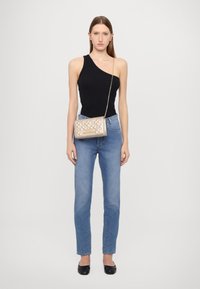 Top nero a spalla unica, jeans azzurri a vita alta e borsa metallizzata trapuntata con tracolla a catena. Le scarpe nere flat completano il look.