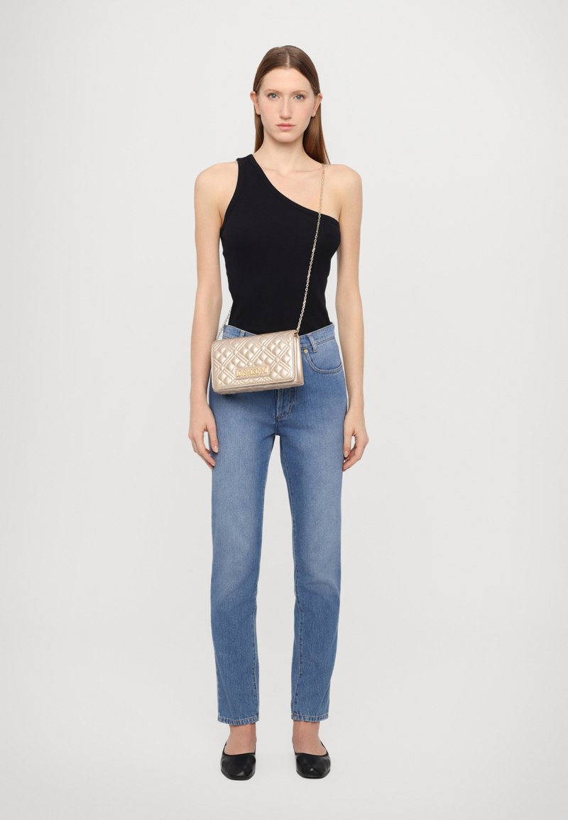 Top nero a spalla unica, jeans azzurri a vita alta e borsa metallizzata trapuntata con tracolla a catena. Le scarpe nere flat completano il look.