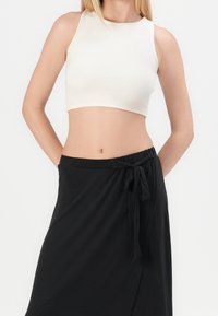 Un crop top blanc à côtes associé à une jupe portefeuille noire avec un lien à la taille. Les tissus semblent lisses et légers.