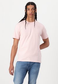 Camiseta de algodón de color rosa claro con mangas cortas, cuello redondo y un corte relajado, combinada con jeans de mezclilla azul. Diseño sencillo sin patrones.
