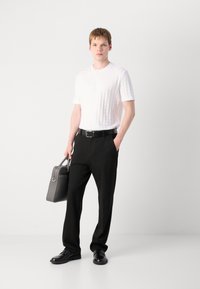 Cămașă albă texturată cu mânecă scurtă, pantaloni negri și pantofi negri. Ținând o geantă gri cu mâner de sus. Siluetă simplă, modernă.