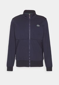 Marineblaue Zip-Jacke aus weichem Stoff, mit Stehkragen, grünem Innenfutter und kleinem Logo auf der Brust.