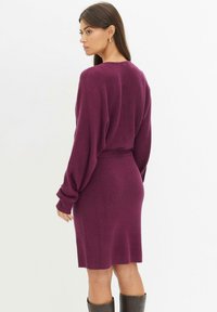 Abito a maglia fitted color marrone bordeaux con maniche lunghe e larghe e una texture a coste. Design semplice, che arriva a metà coscia con una leggera svasatura in vita.