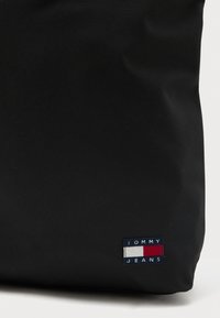 Τσάντα tote από μαύρο ύφασμα με μικρό κεντημένο λογότυπο Tommy Jeans σε μπλε, άσπρο και κόκκινο στην κάτω αριστερή περιοχή.