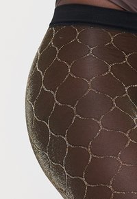 Schwarze transparente Leggings mit einem geometrischen goldenen Muster. Sie verfügen über eine glatte, elastische Textur und einen schwarzen elastischen Bund.