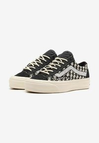 Sneakers a pattern bianco e nero con una tomaia texturizzata, lacci crema e una suola in gomma. Il lato presenta una striscia bianca caratteristica.
