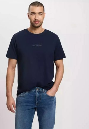 Granatowy t-shirt z krótkim rękawem wykonany z bawełny, z okrągłym dekoltem. Posiada subtelny nadruk tekstowy z przodu. W połączeniu z jasnoniebieskimi dżinsami.