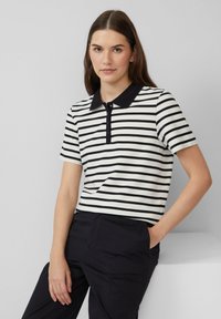 Gestreepte polo-shirt in zwart en wit met korte mouwen, een zwarte kraag en een placket met vier knopen. Draagt een zwarte broek.