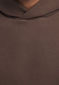 Un hoodie en tissu brun avec une capuche large et une texture douce, au design simple sans motifs ni détails matériels visibles.