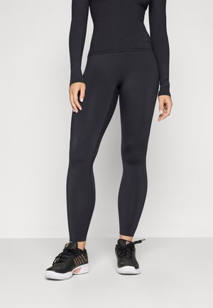 Haut de sport à manches longues noir avec texture côtelée, associé à des leggings noirs fuselés. Porté avec des chaussures de sport noires avec des accents roses.