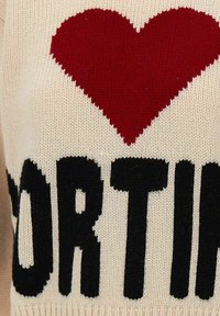 Tissu tricoté crème avec un grand cœur rouge au-dessus de lettres noires en gras montrant partiellement le mot "NORTH".