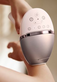 Appareil portable avec un dessus rose et une section inférieure argentée, comportant des boutons pour l'opération. Il est positionné près du bras d'une personne.