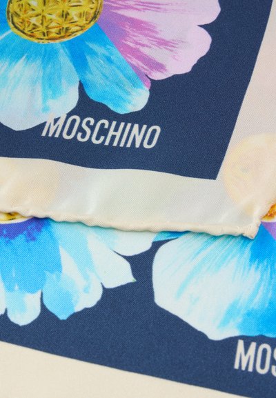 Tissu en soie avec un imprimé floral bleu et violet et des détails dorés, avec le nom de la marque Moschino en blanc sur un fond bleu foncé.