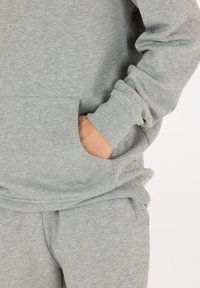 Grijze sweatshirt en sweatpants, gemaakt van zachte stof. Heeft een vo zak en ribgebreide manchetten, met een gladde, uniforme textuur.