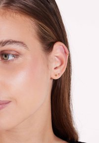 Gouden oorbellen met twee ronde studs in verschillende maten en een kleine hoepel in het bovenste gedeelte van het oor, benadrukt tegen een lichte huid.