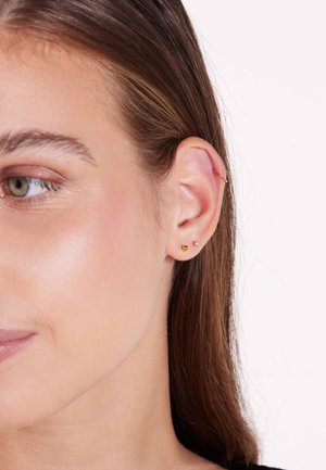 Gouden oorbellen met twee ronde studs in verschillende maten en een kleine hoepel in het bovenste gedeelte van het oor, benadrukt tegen een lichte huid.